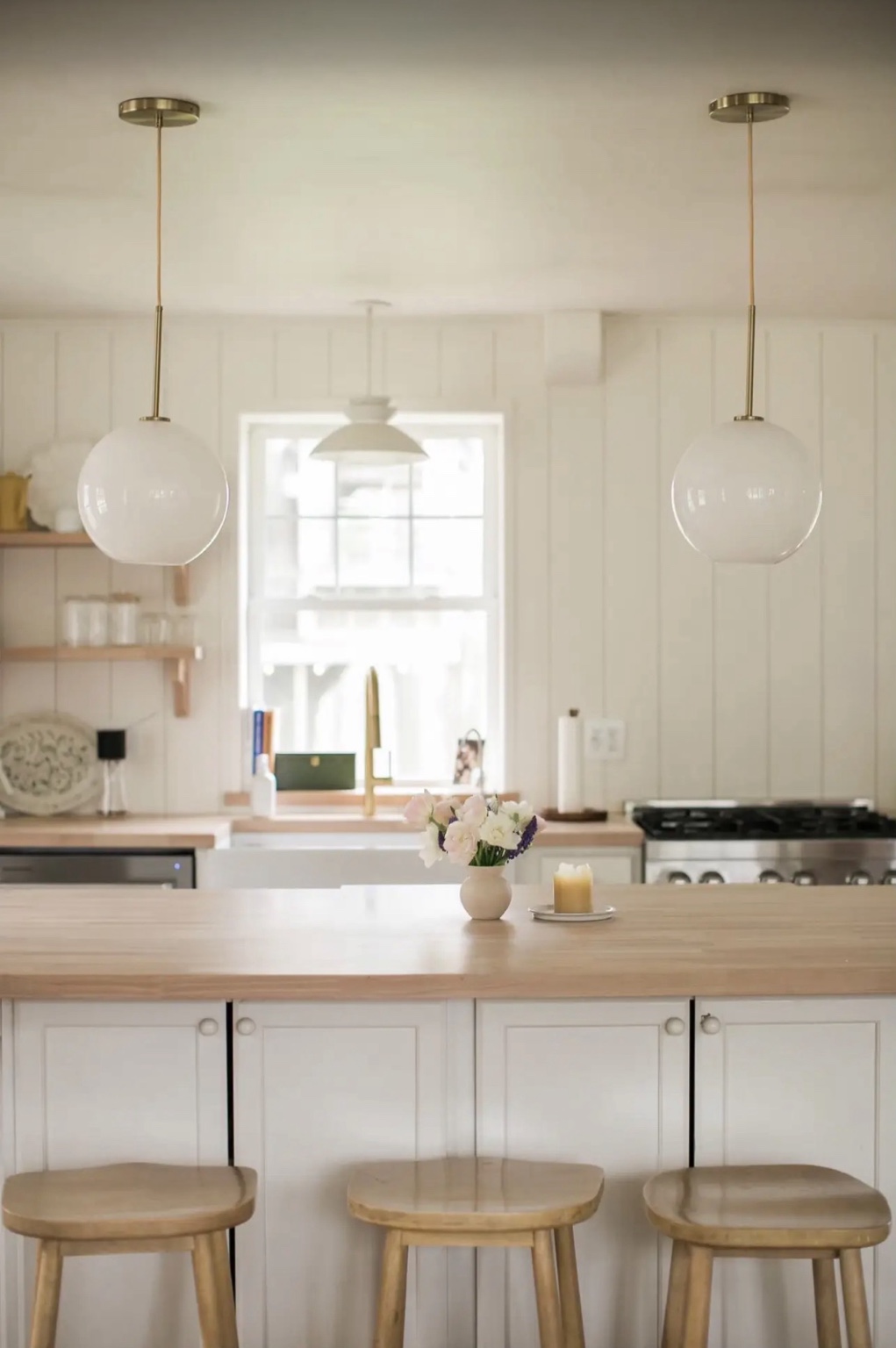 Warm white Bahrke Built kitchen with a natural wood island and globe pendant lights